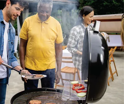 Three people gathered around a barbecue in a garden.